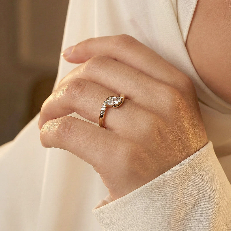 Hand wearing a rose gold ring with a pear-shaped diamond on a neutral background