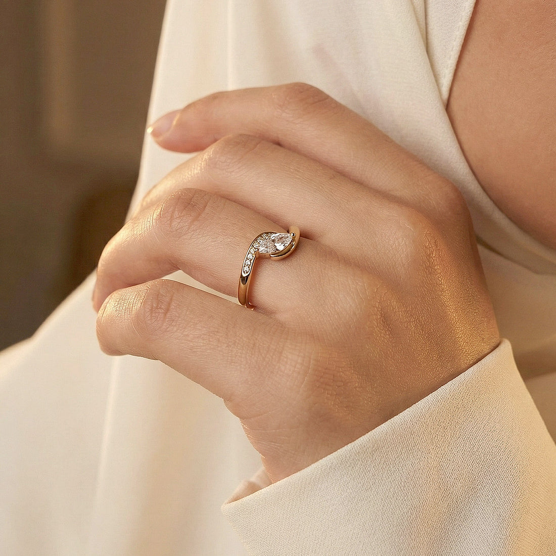 Hand wearing a rose gold ring with a pear-shaped diamond on a neutral background